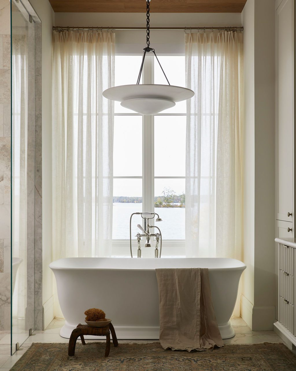 Bathroom with sheers overlooking a lake behind a freestanding tub