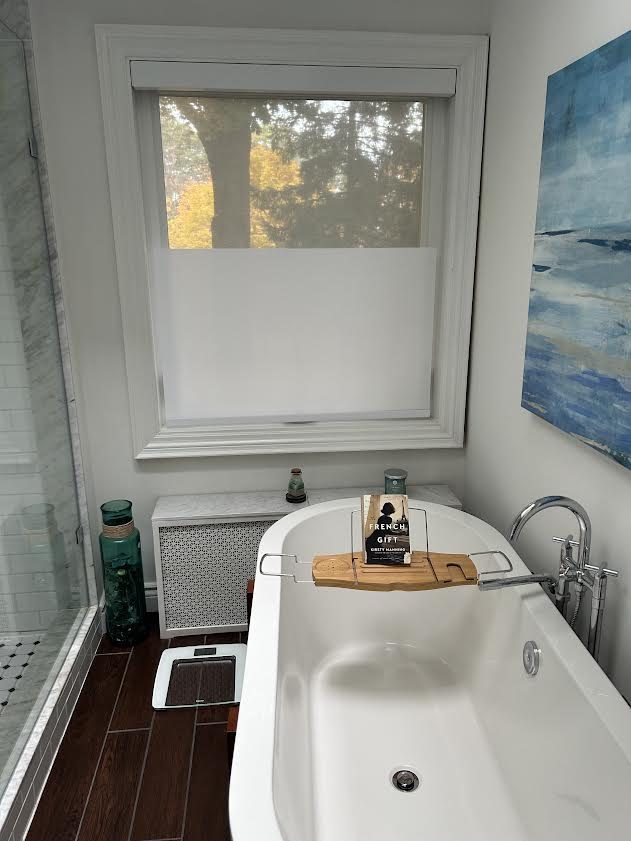 Bathroom window above a freestanding tub with a white shade raised from the sill