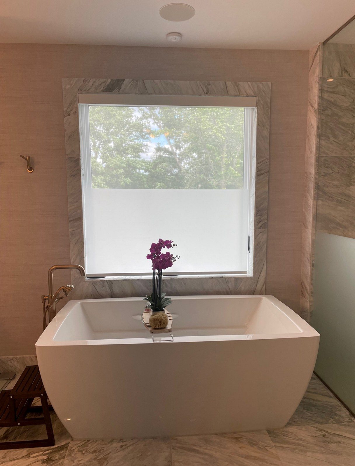 Bathroom with a bottom-up shade covering the lower half of the window behind a freestanding tub