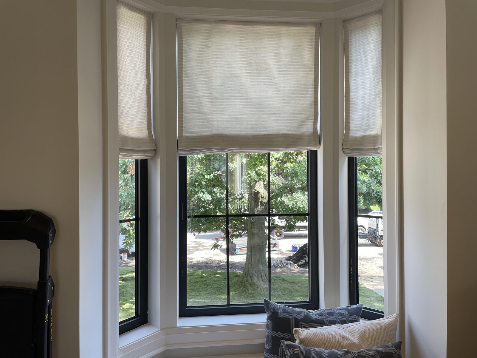 Bay window with three flat-fold linen Roman shades above a cushioned window seat