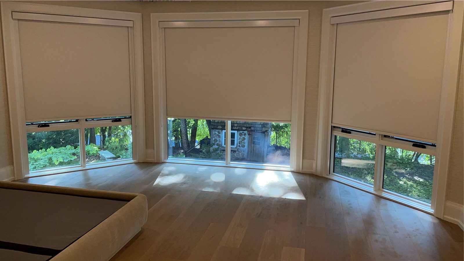 Bay of three windows with cream roller shades lowered to the same line