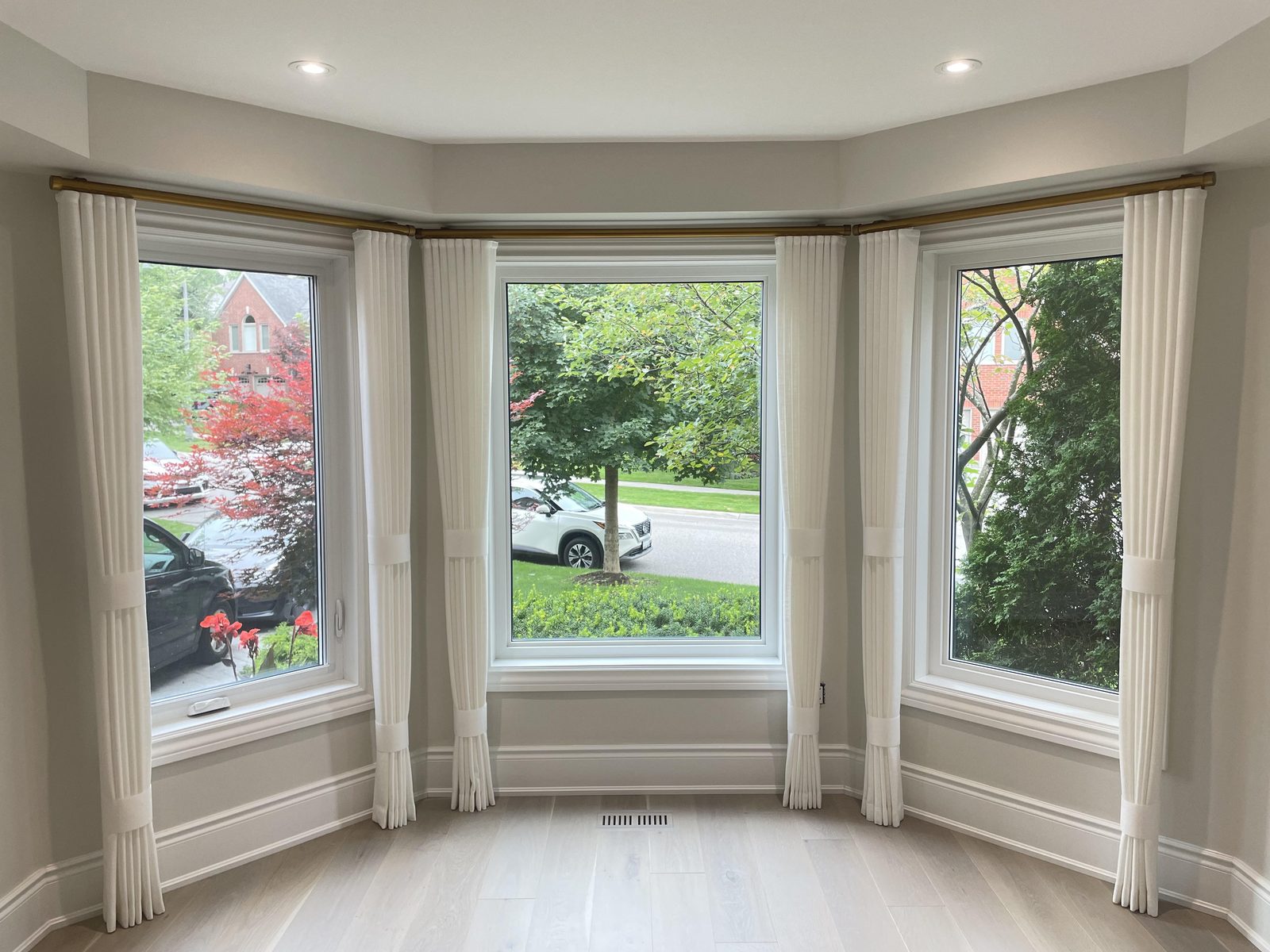 Bay window with ivory pleated drapery panels held back at each of three windows