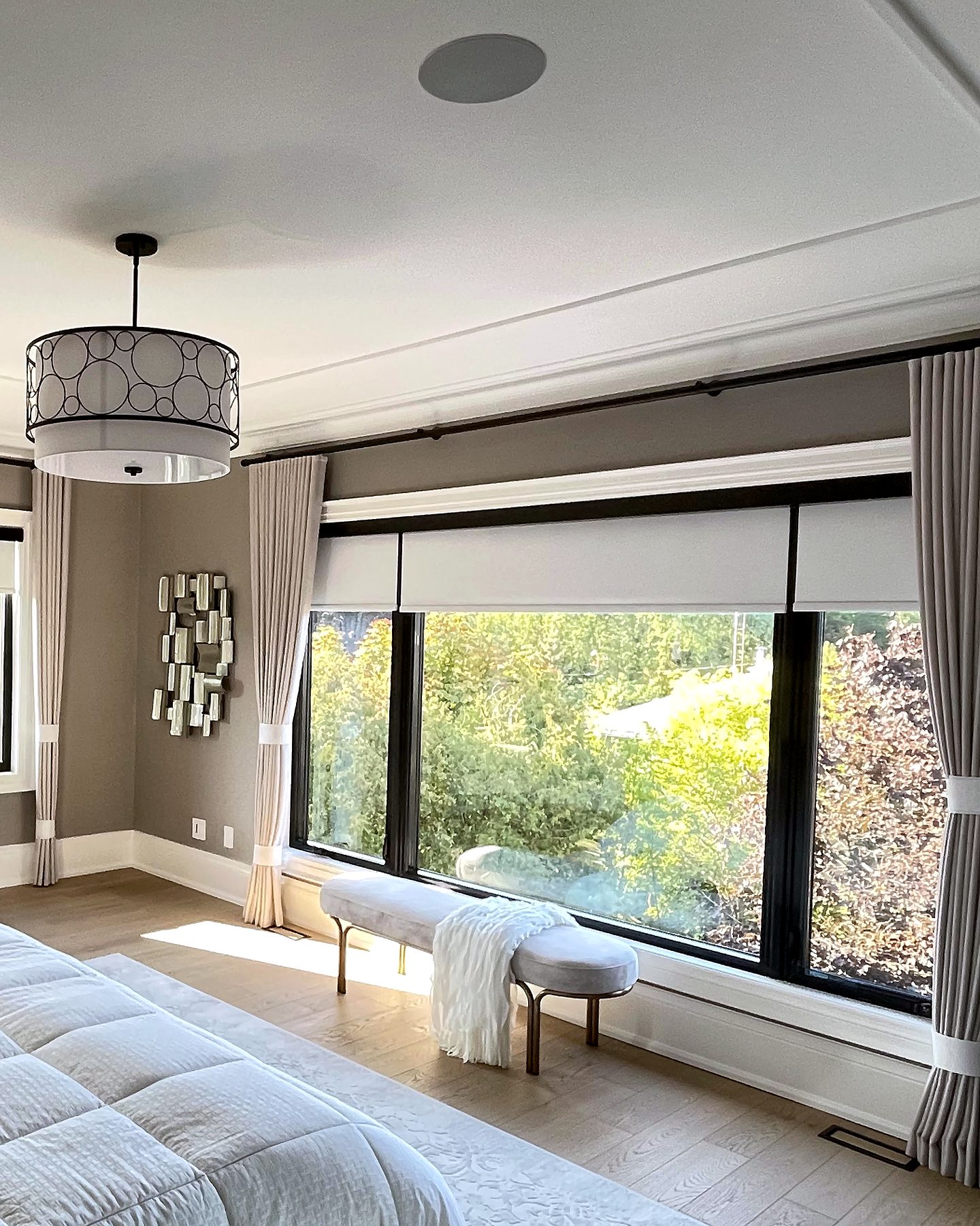 Principal bedroom with drapery panels and roller shades on a wide window