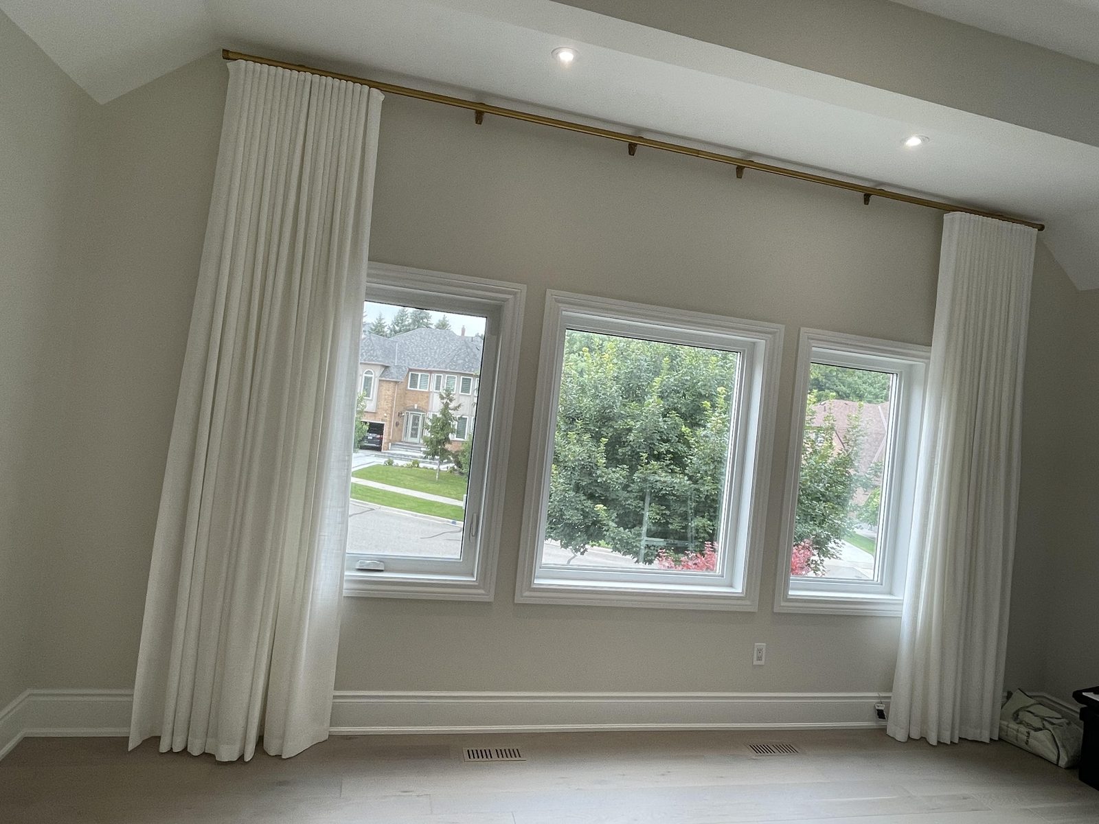 Bedroom with ivory pinch-pleat drapery panels at each end of a run of three windows