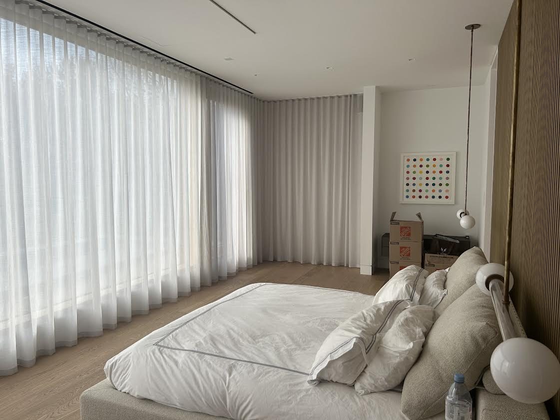 Bedroom with white ripple-fold sheers at the window wall and greige ripple-fold drapery on the return wall