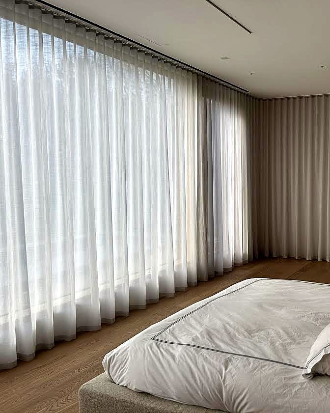 Bedroom with wall-to-wall ripple-fold sheers layered over taupe opaque drapery