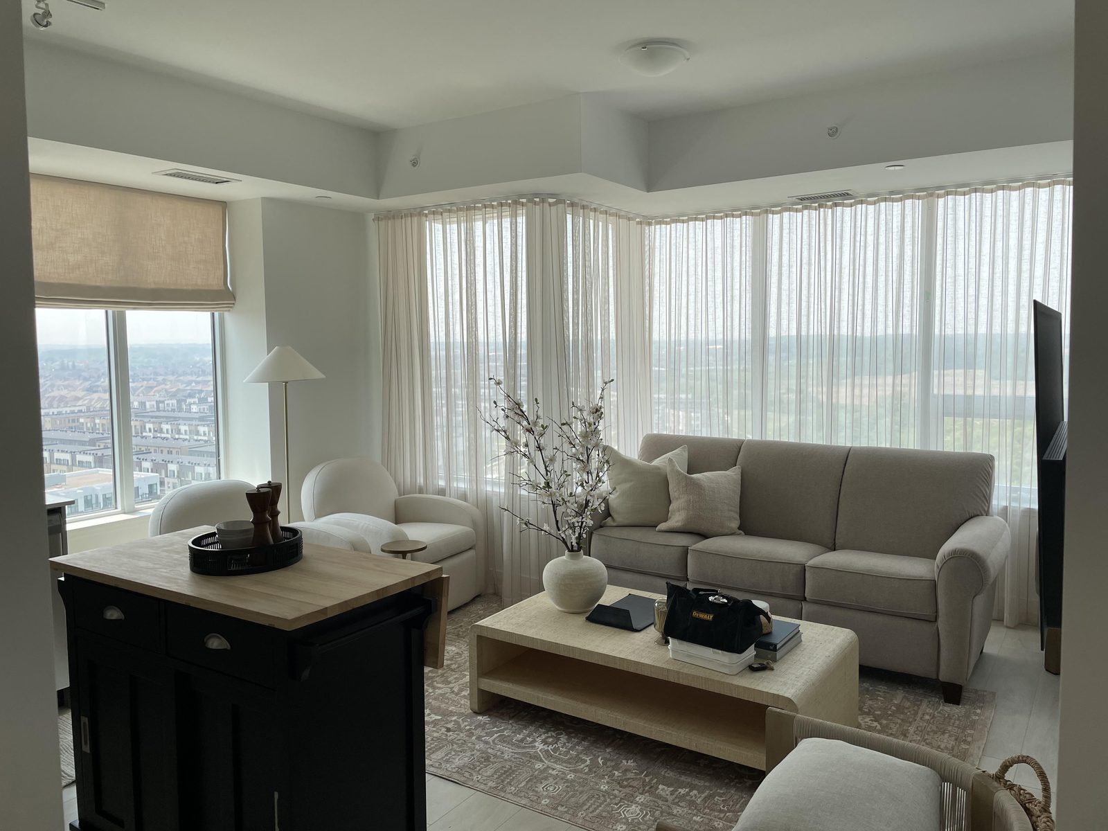 Condo living room with wall-to-wall sheers and a linen Roman shade at the kitchen window