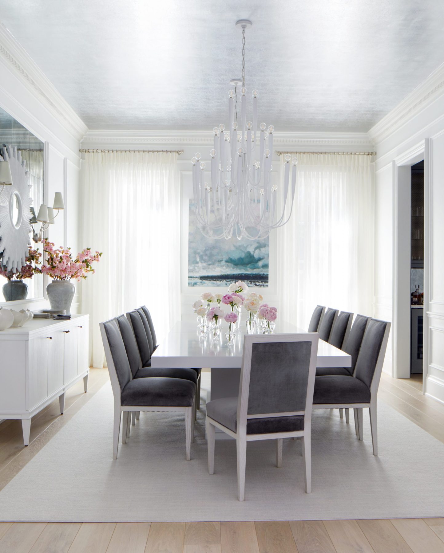 Dining room with white pinch-pleat sheer panels drawn across two tall windows