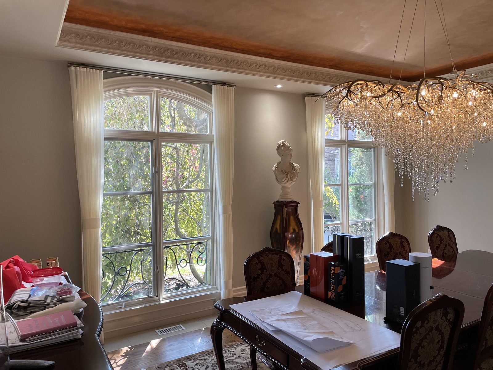 Dining room with cream sheer panels flanking an arched window beneath a crystal chandelier