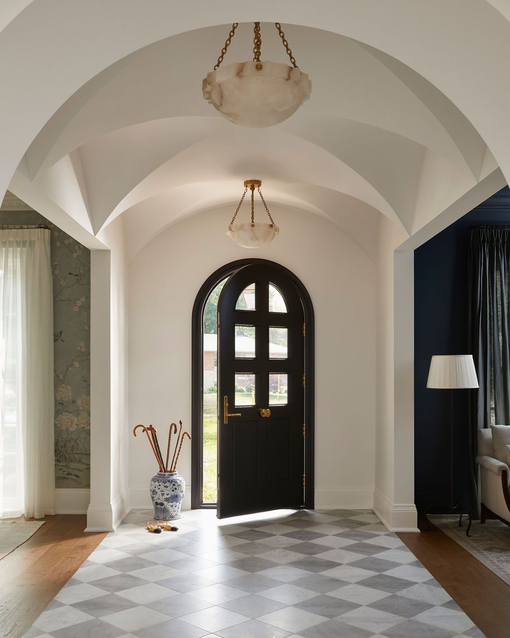Vaulted entry with an arched black front door, sheer panels in the room to the left and dark pleated panels to the right