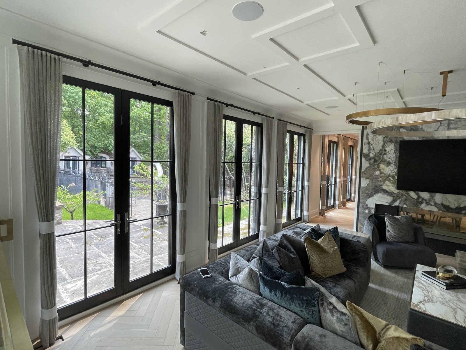 Family room with grey pleated drapery panels, banded in ivory, at black steel doors