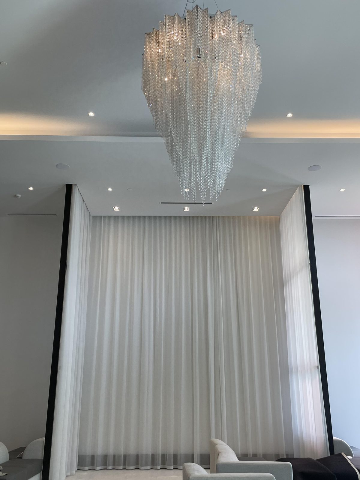 Great room with full-height ivory sheers on a ceiling track beneath a large crystal chandelier