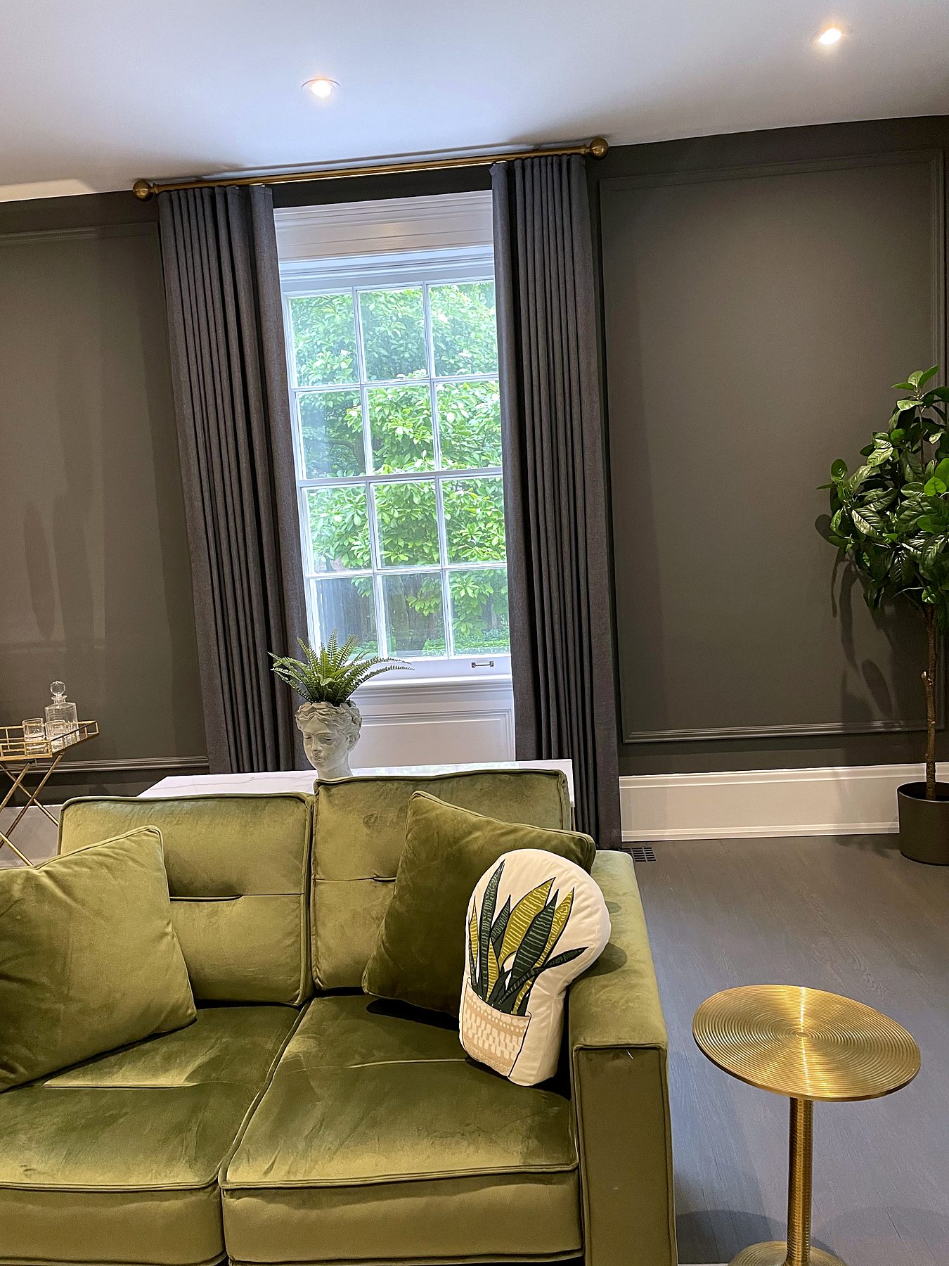 Grey drapery panels on a brass rod above a green velvet sofa