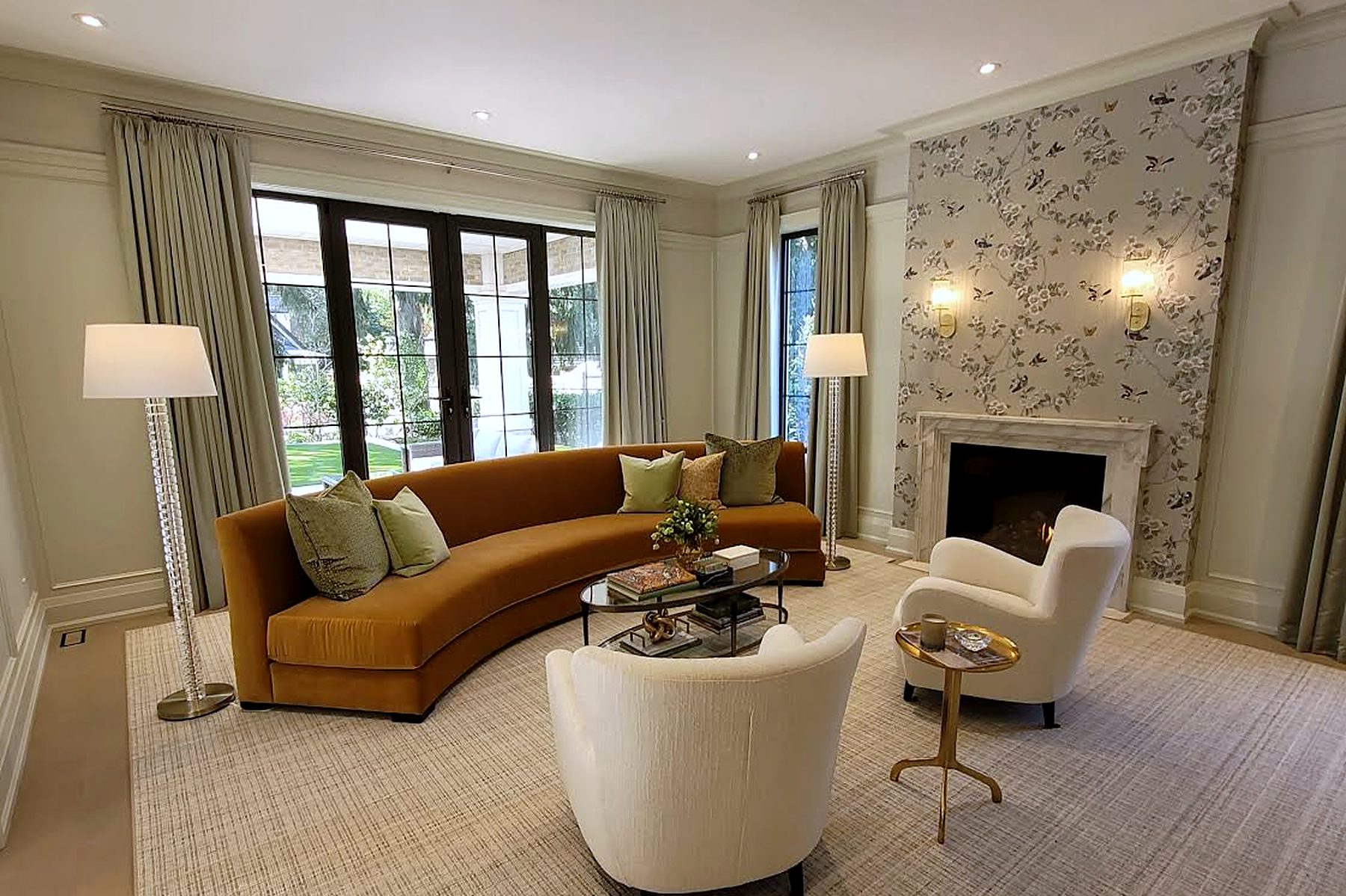 Living room with tailored drapery, curved velvet sofa and floral wallpaper