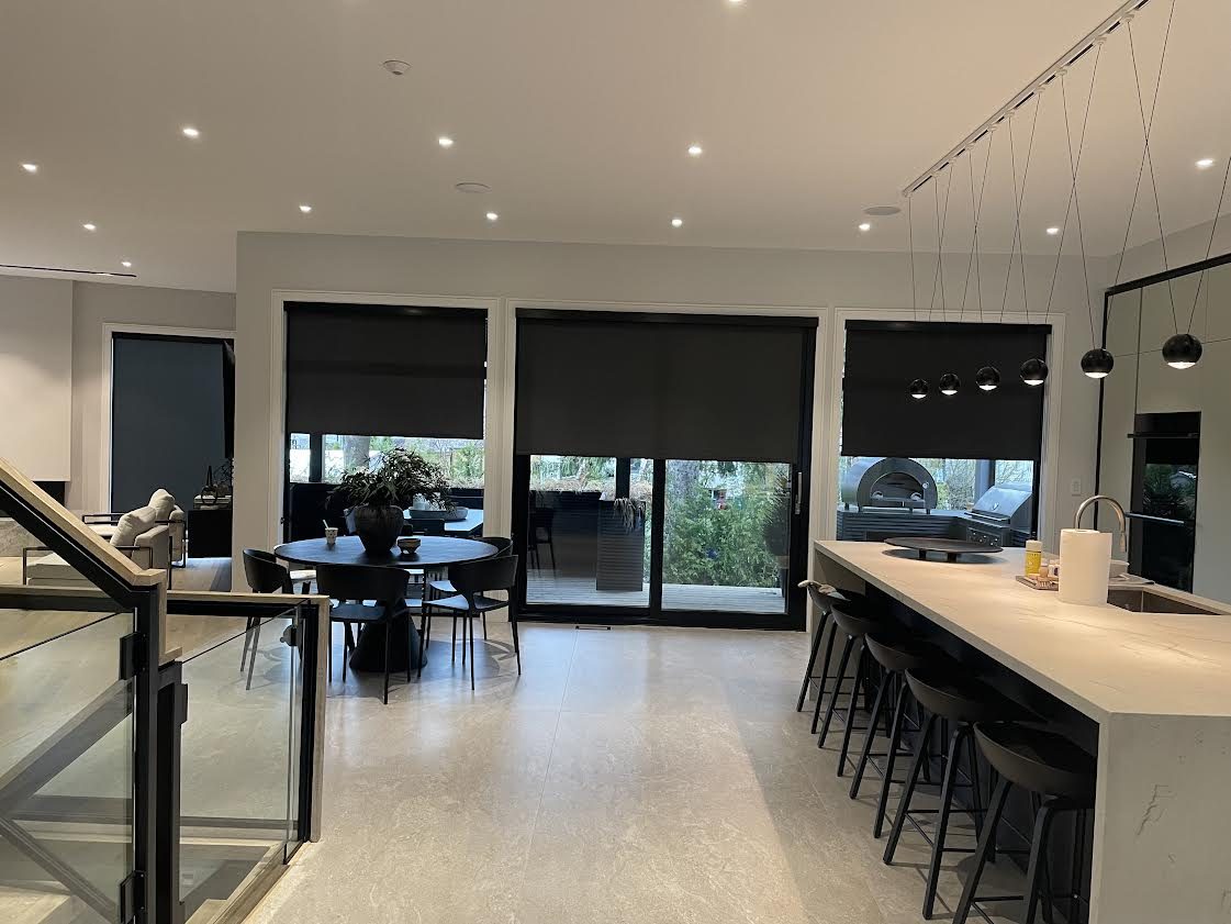 Open-plan kitchen and dining area with black roller shades on the windows and patio doors