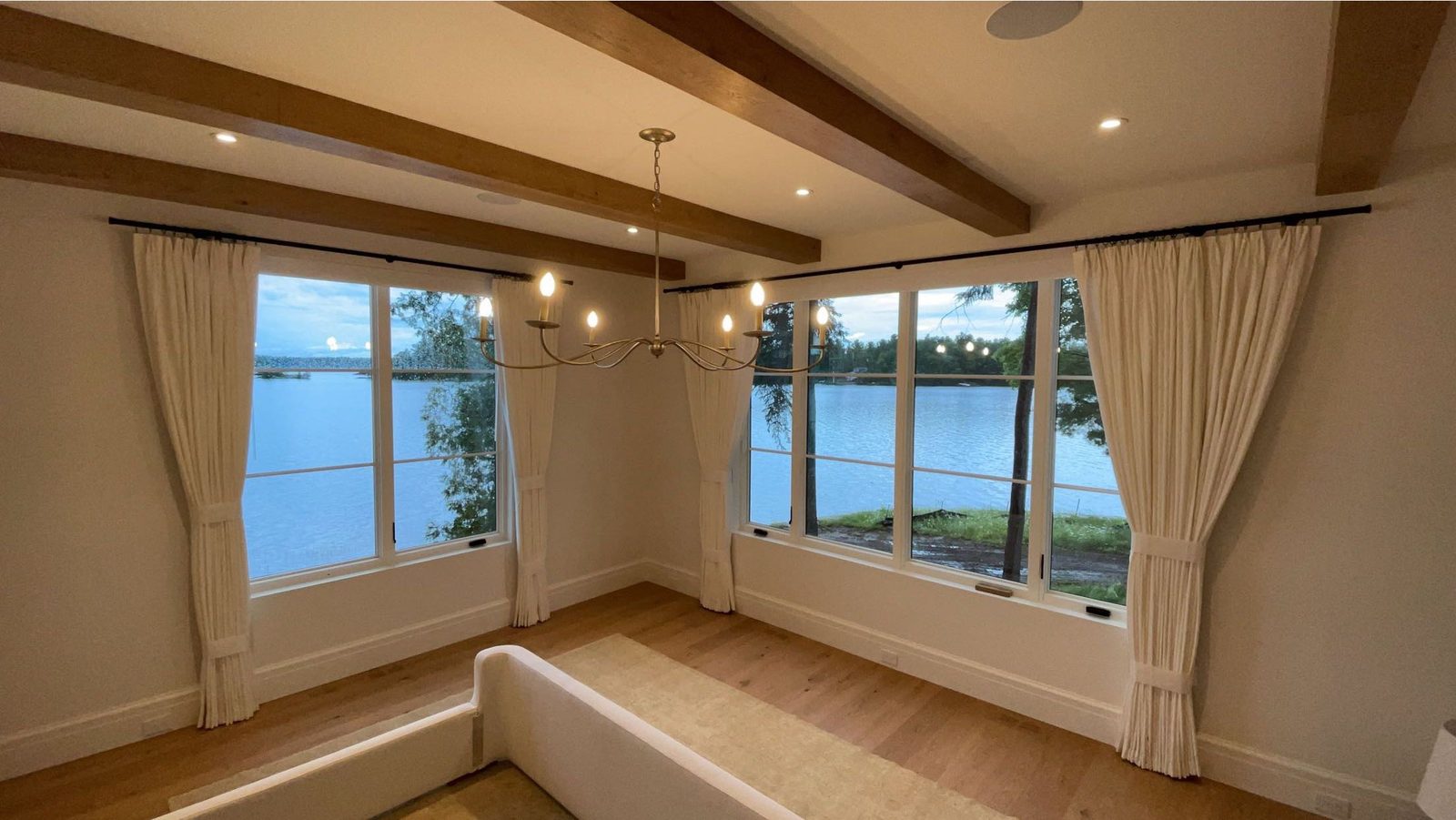 Lakeside room with ivory pleated drapery panels tied back at corner windows