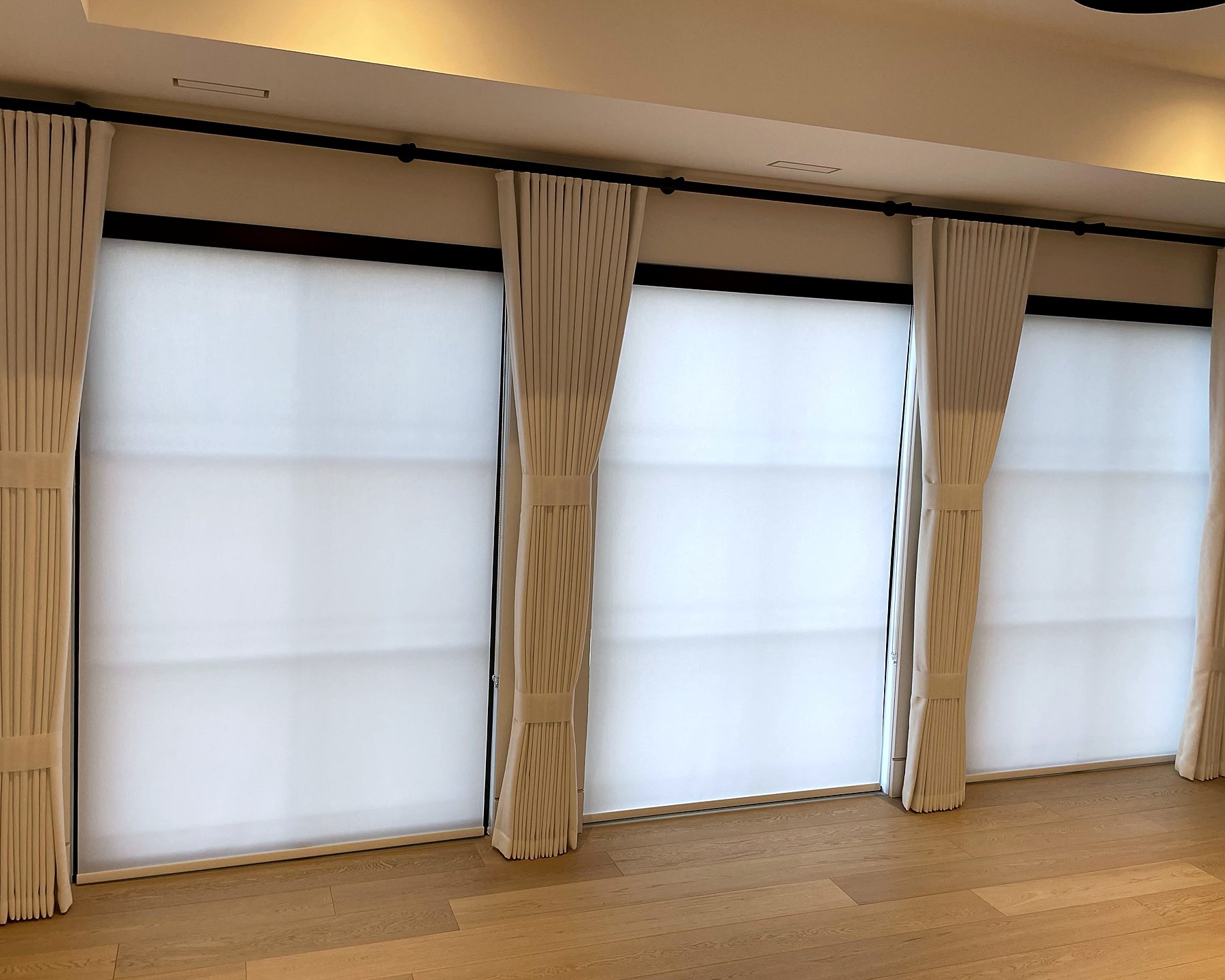 Three windows with light-filtering roller shades and ivory pleated drapery panels
