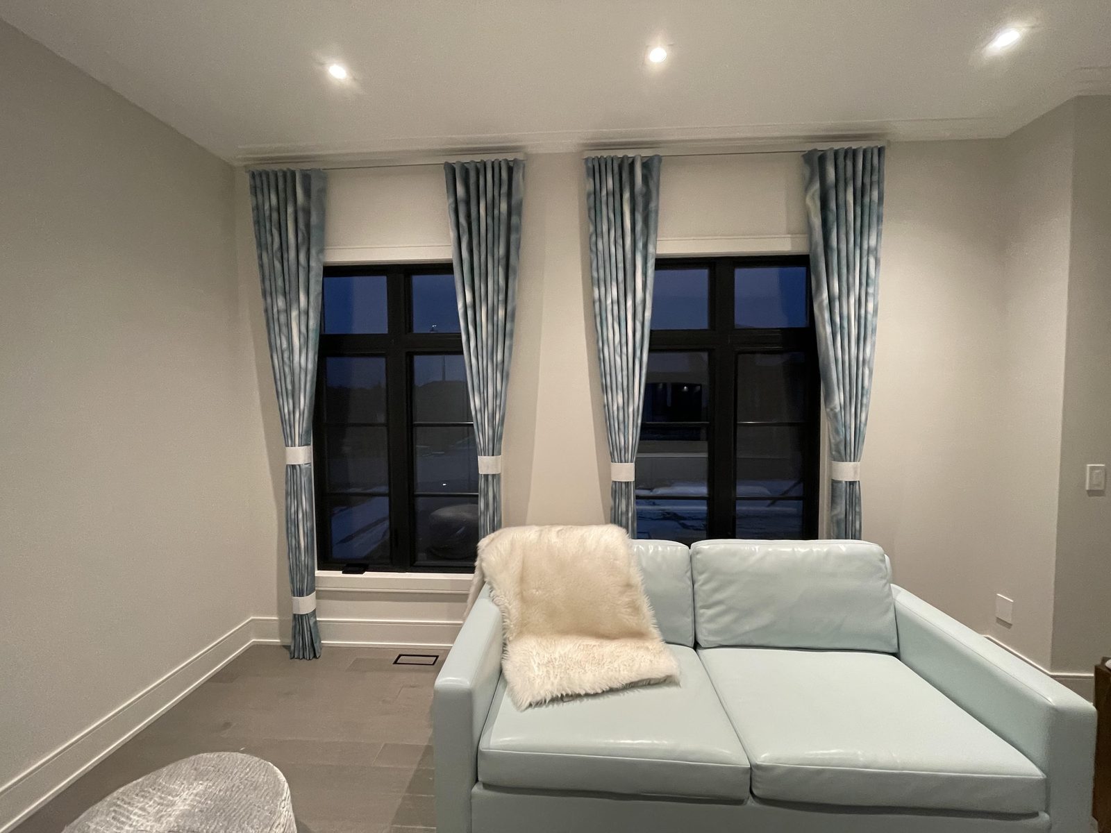 Living room with blue patterned drapery panels tied back at two black-framed windows