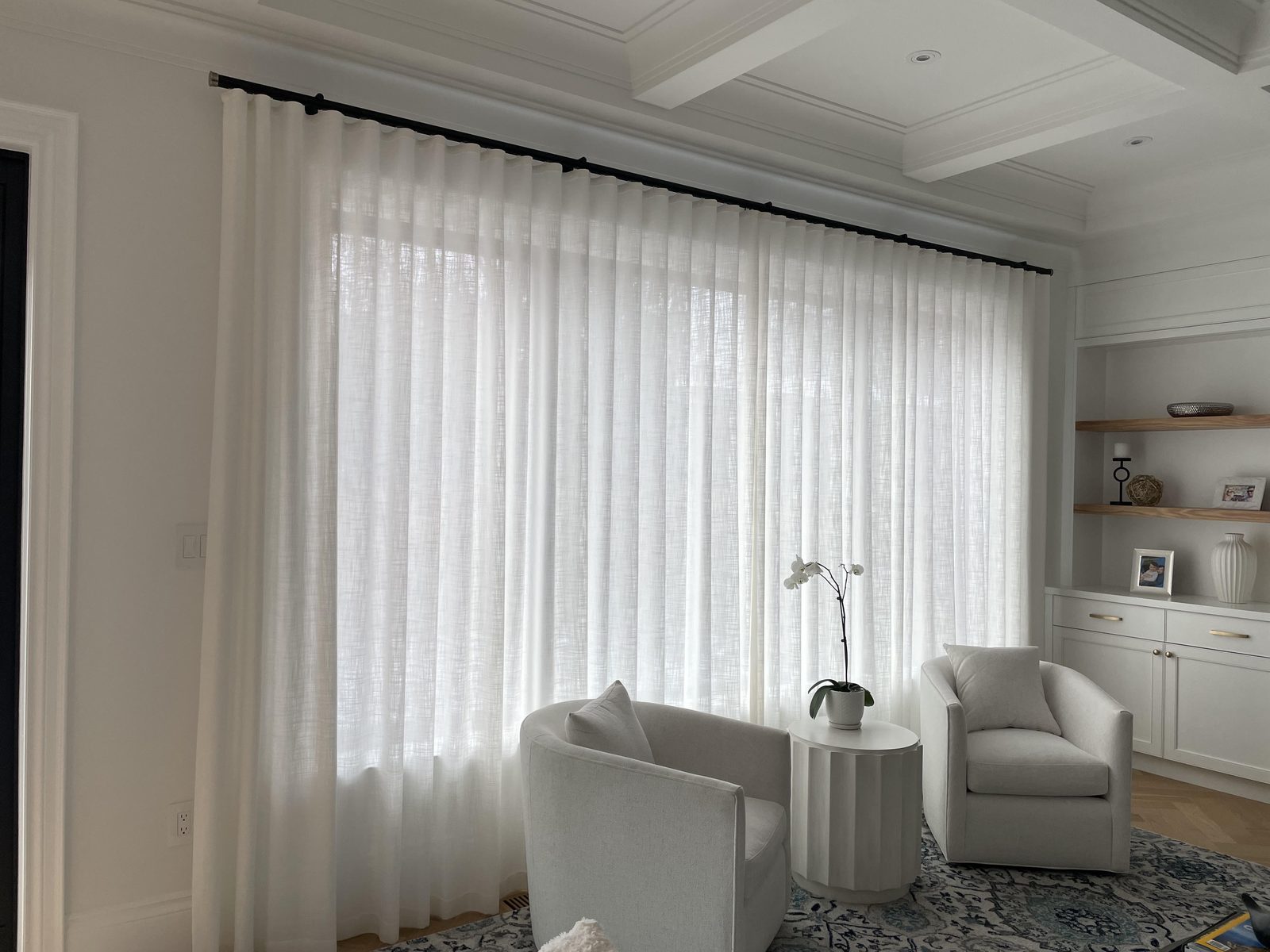 Living room with white sheers spanning a wide window on a black rod