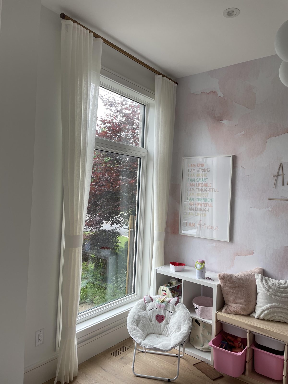 Child's room with white sheer drapery panels on a wood rod at a tall window