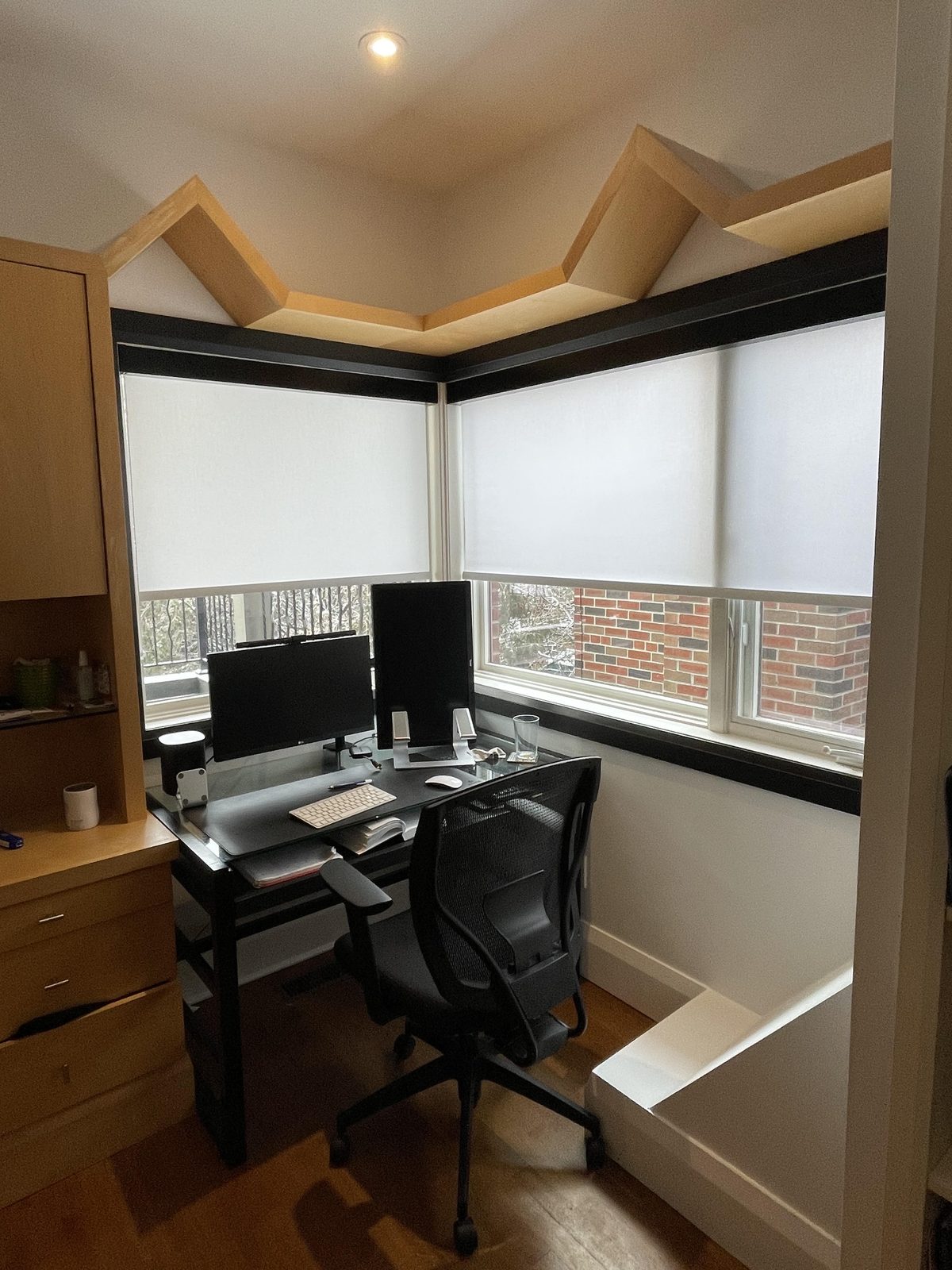 Home office desk in a corner with white light-filtering roller shades on both windows