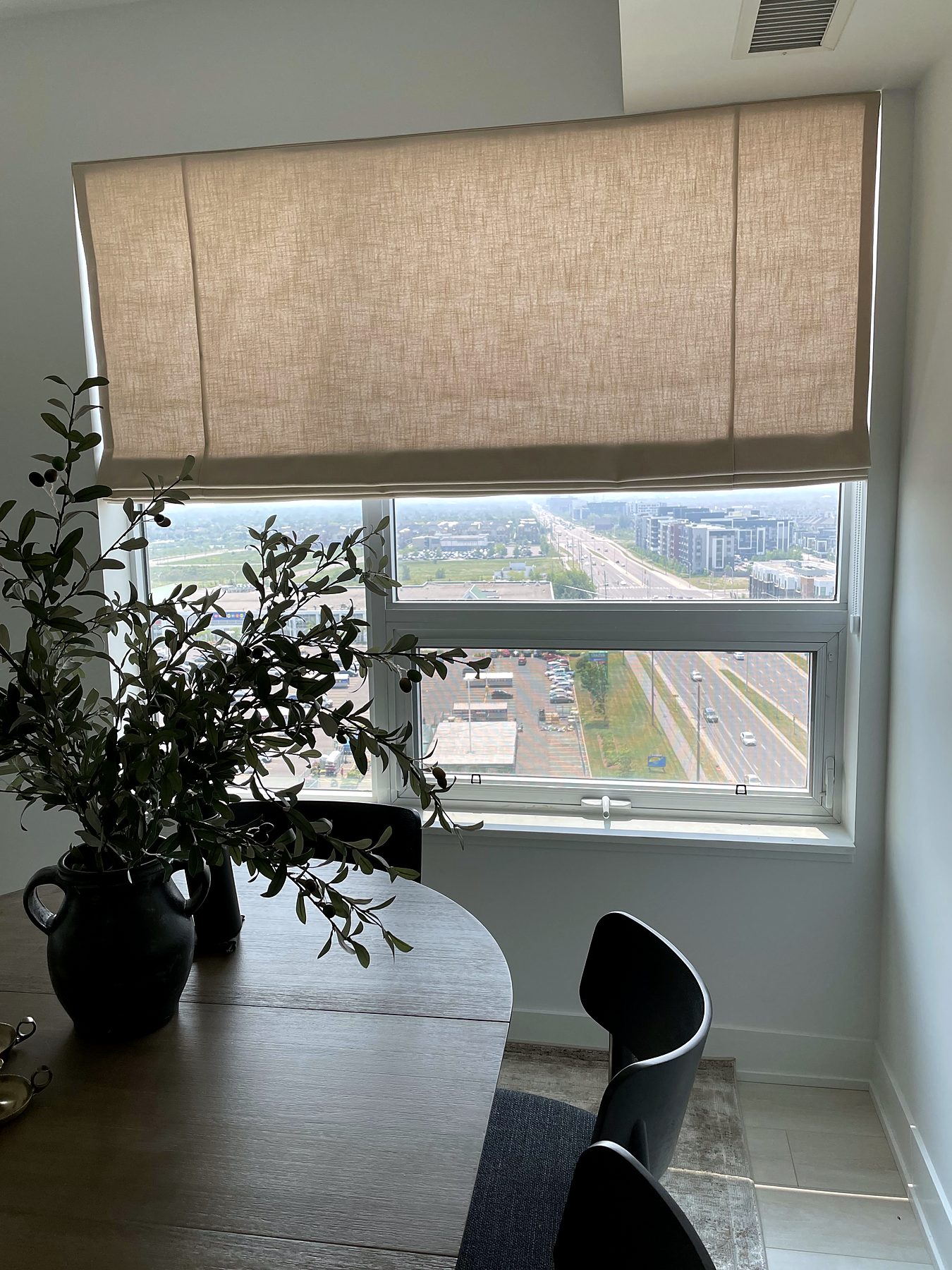Condo dining area with a linen Roman shade over a high-rise view