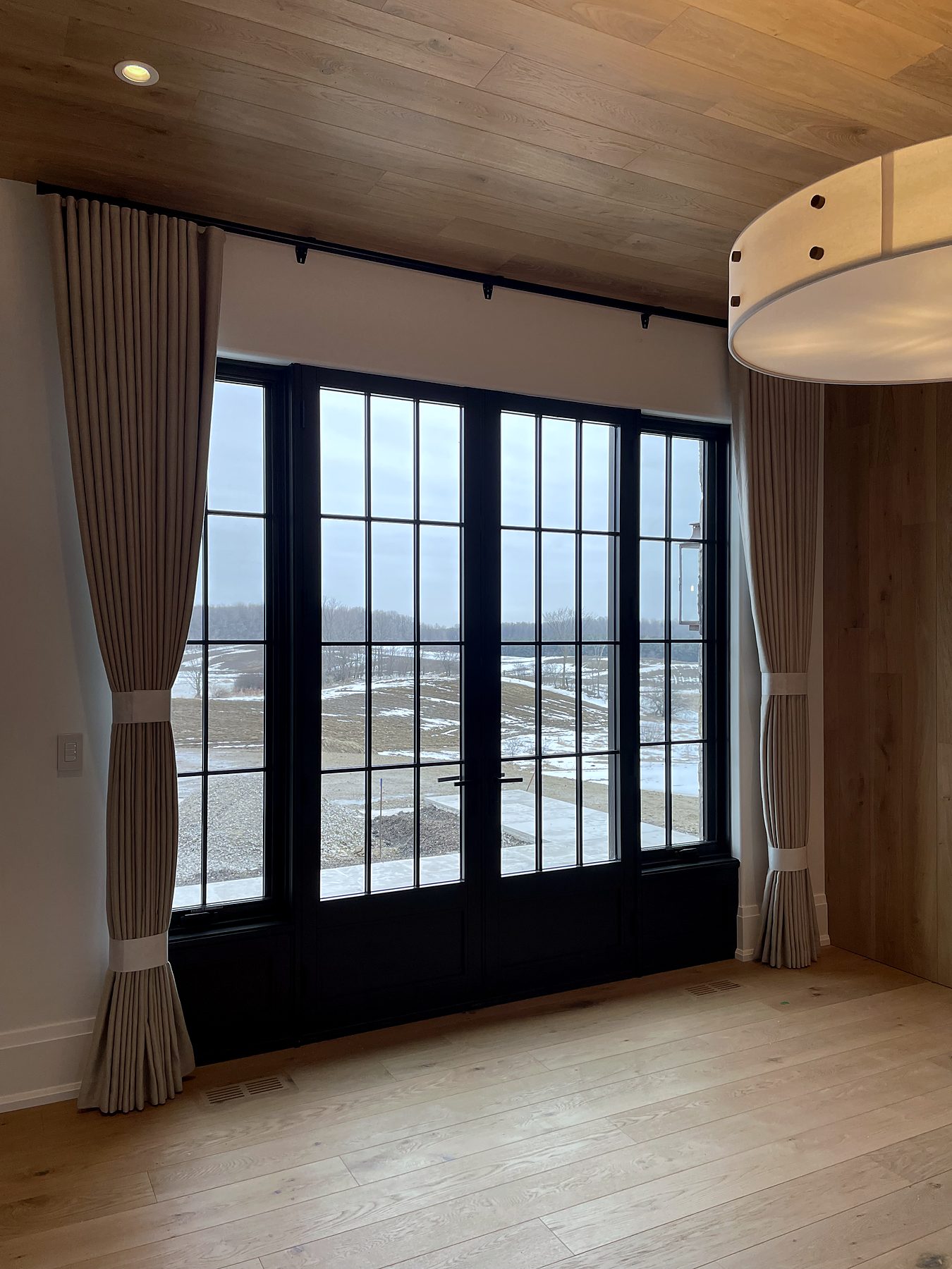 Black steel doors with linen drapery under a wood ceiling